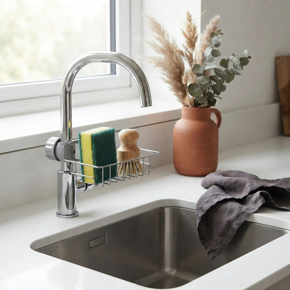 A sink caddy organiser holding a sponge and scrubber on a clean white countertop next to a kitchen sink.